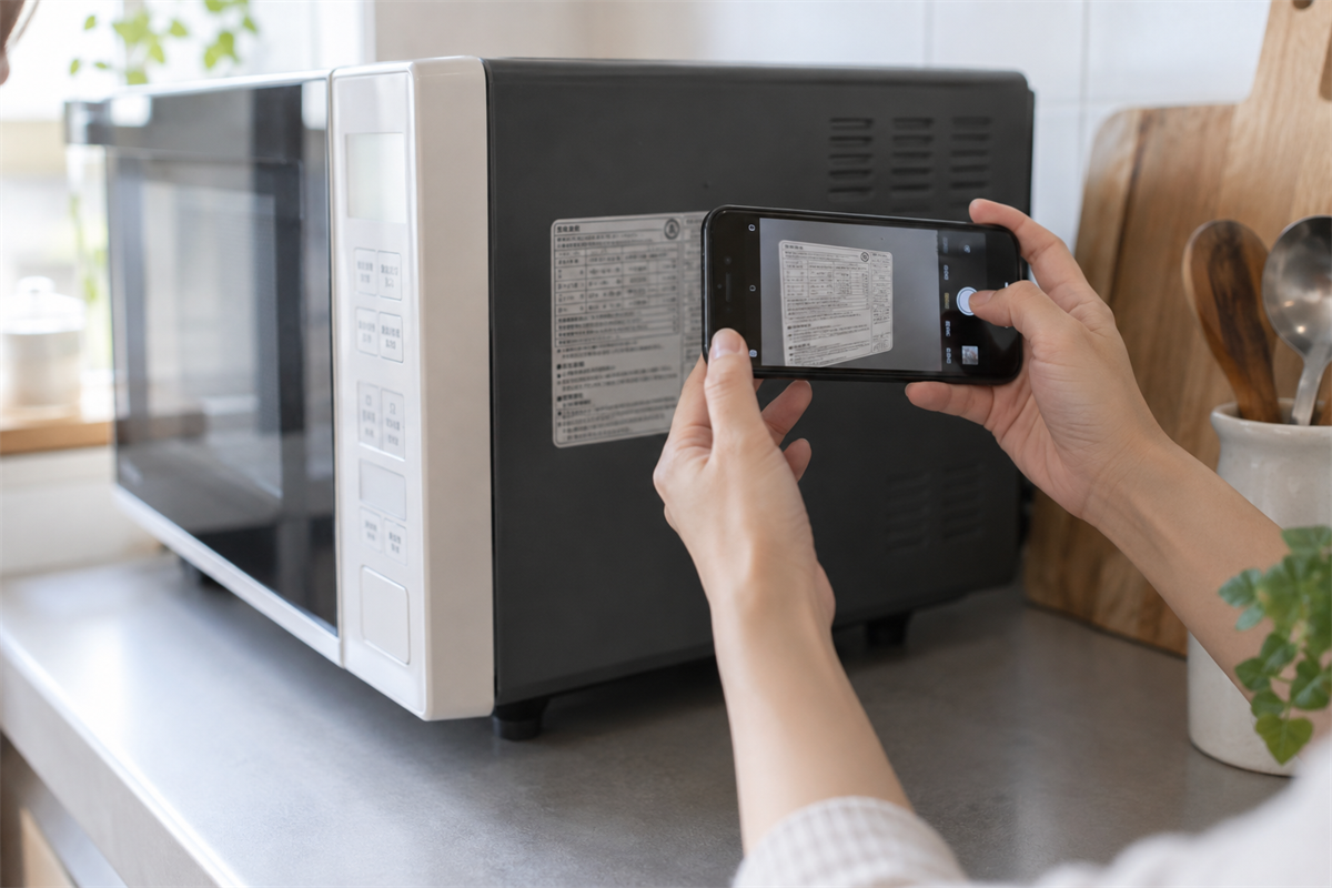 電子レンジの側面にある銘板をスマートフォンで確認する手元